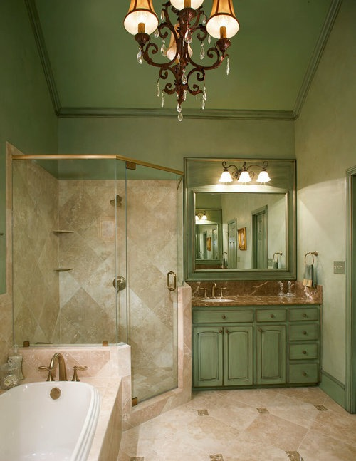 Elegant bathroom with green vintage-style cabinetry, chandelier lighting, glass shower, and a soaking tub.