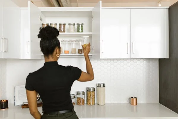 Woman reaching into a neutral-tone cabinet in a modern white kitchen