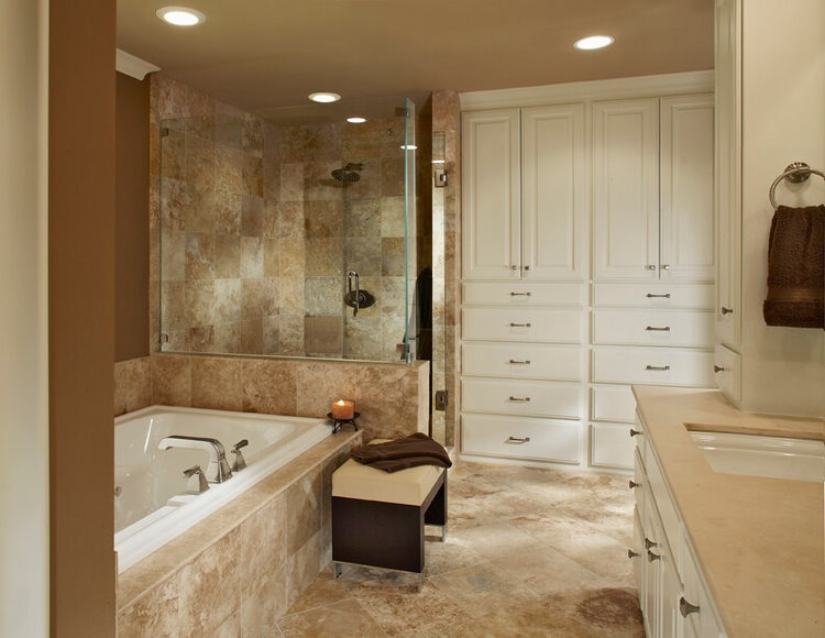 a small bathroom with stone tiles, a tub, a walk-in shower, and white built-in cabinets and drawers